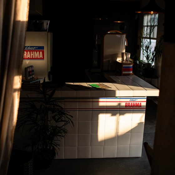 O balcão do bar, revestido de azulejo branco com as faixas vermelha e azul do Chopp Brahma, cortado por uma faixa de sol do fim da tarde.