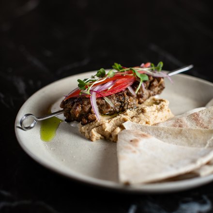 Kafta de cordeiro sobre húmus, com salada de cebola e tomate e triângulos de pão sírio ao lado.