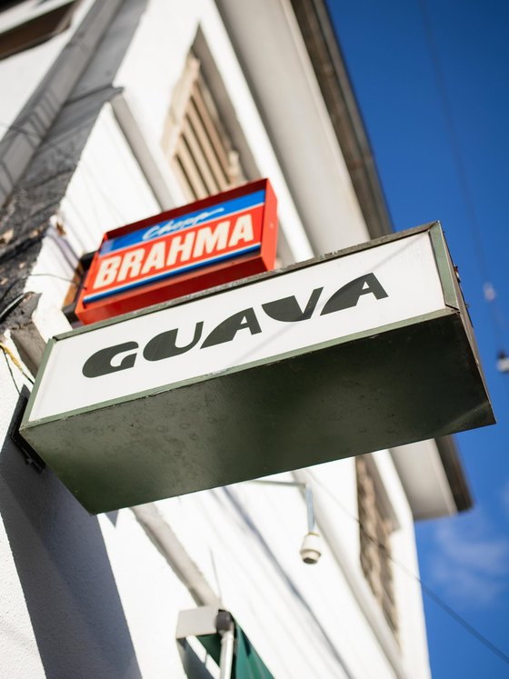 O letreiro luminoso do Guava, caixa verde com o nome em preto sobre fundo branco, e uma placa de Chopp Brahma logo acima, contra o céu azul.