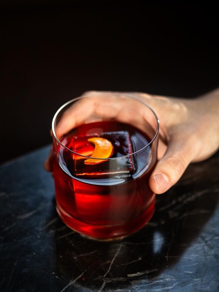 Negroni num copo baixo com uma pedra de gelo grande, sobre mármore escuro.